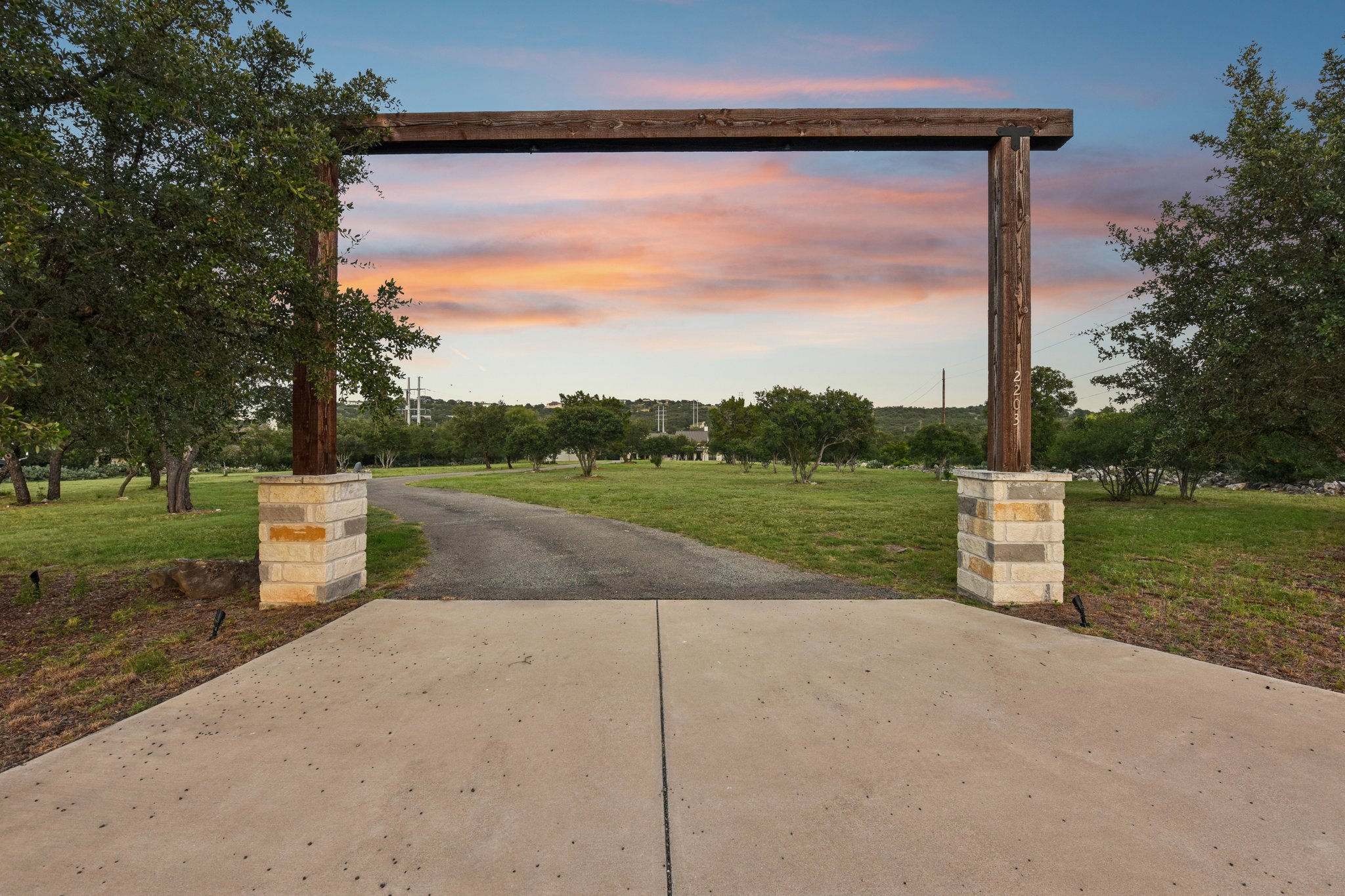 2203 Improver Road Spicewood, TX 78669 - Photo 9 of 38 Enter this private estate through a grand wooden archway, revealing a long, inviting driveway amidst a verdant landscape.