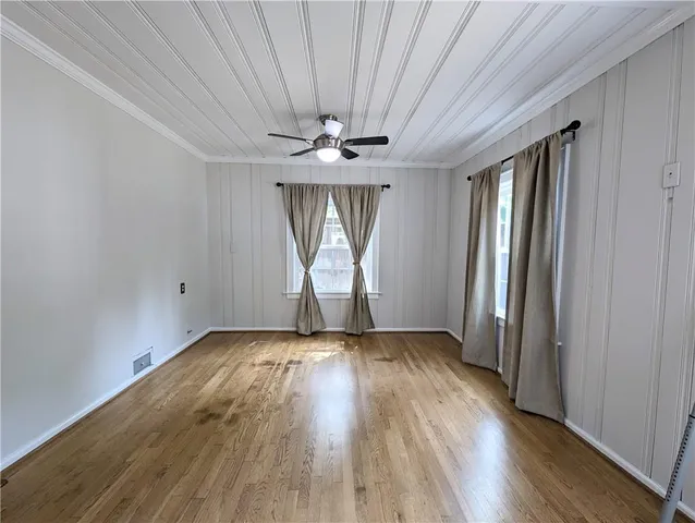 an empty room with wooden floor chandelier fan and windows
