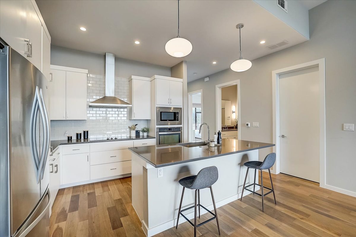 5921 Hiline Road, Unit 1204 Austin, TX 78734 - Photo 15 of 36 Kitchen with appliances with stainless steel finishes, a kitchen island with sink, a kitchen breakfast bar, wall chimney range hood, and white cabinetry