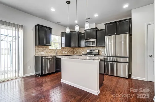 a kitchen with stainless steel appliances granite countertop a refrigerator a sink dishwasher a oven and a large window with wooden floor