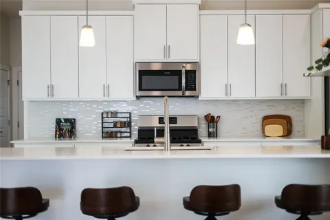 a kitchen with stainless steel appliances granite countertop a refrigerator a stove top oven a sink dishwasher and white cabinets with wooden floor