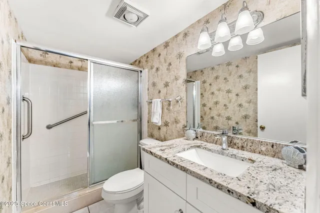 a bathroom with a granite countertop sink a toilet a mirror a vanity and shower