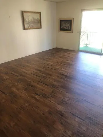 a view of an empty room with wooden floor and a window