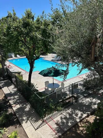 a view of a patio with table and chairs under an umbrella with large trees