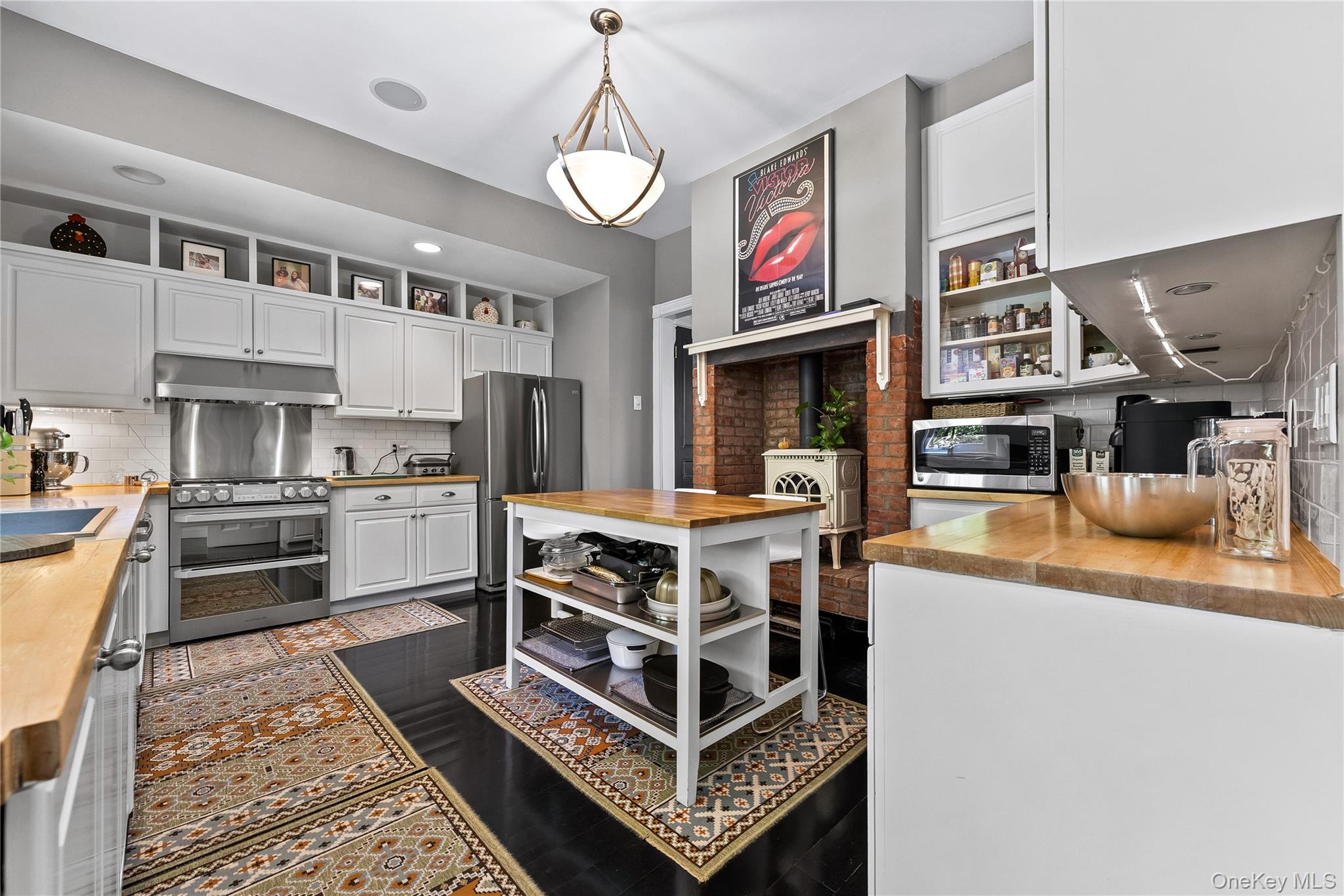 19 Howe Place Bronxville, NY 10708 - Photo 14 of 37 Gourmet kitchen featuring a stainless steel gas range, coordinating refrigerator, white shaker cabinetry with open shelving, wood-finish countertops, and a brick-surround fireplace