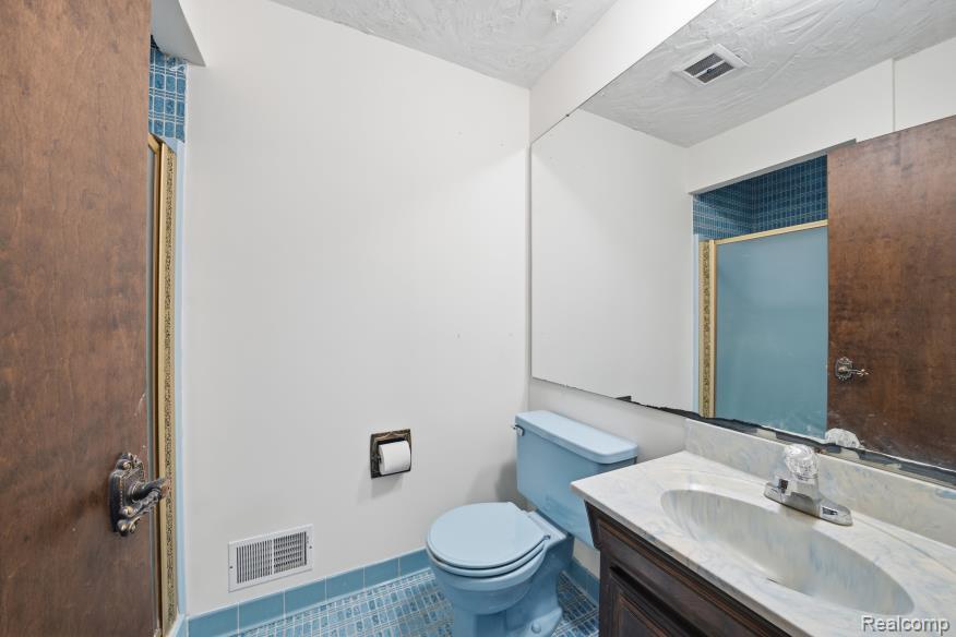 7020 Rattalee Lake Road Clarkston, MI 48348 - Photo 36 of 47 Bathroom featuring a vanity with a white countertop and integrated sink, a large wall-mounted mirror, and a blue toilet