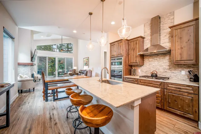 a kitchen with stainless steel appliances granite countertop a stove a sink a oven a dining table and chairs with wooden floor