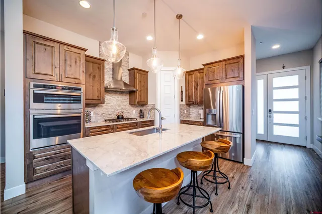 a kitchen with stainless steel appliances kitchen island granite countertop a stove a refrigerator a oven a sink a dining table and chairs with wooden floor