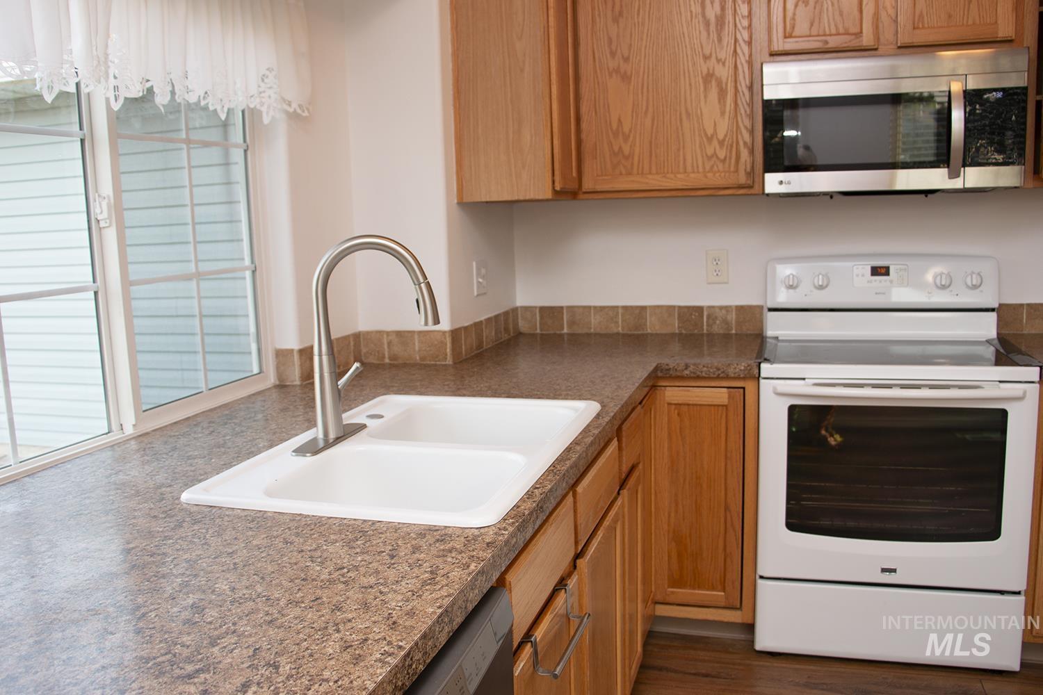 16559 Bayou Way Caldwell, ID 83607 - Photo 10 of 20 Kitchen featuring a double basin sink with a gooseneck faucet, light wood cabinetry, stainless steel microwave, and white range