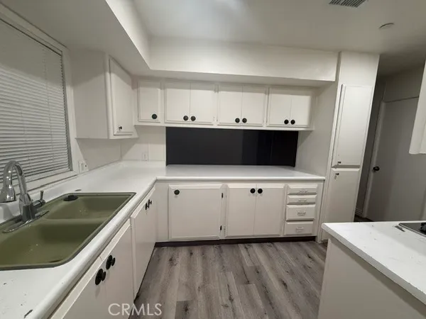 a kitchen with a sink dishwasher and white cabinets with wooden floor