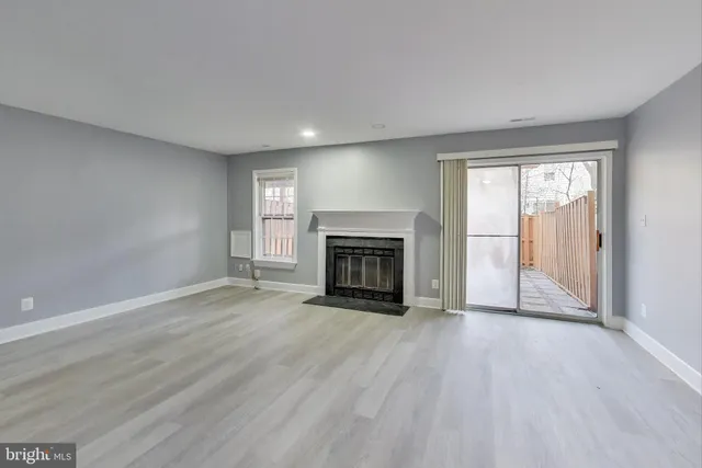 an empty room with wooden floor fireplace and windows