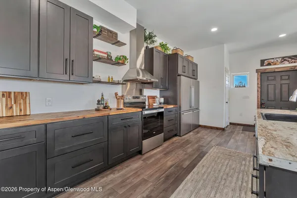 a kitchen with stainless steel appliances kitchen island granite countertop a sink dishwasher a stove a refrigerator and a dining table with wooden floor