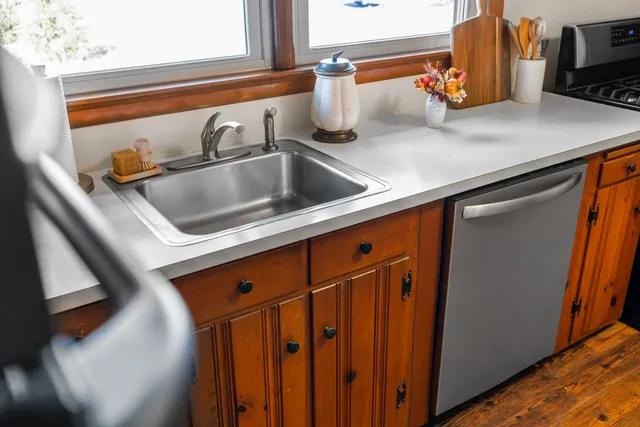 a kitchen with stainless steel appliances a stove a sink dishwasher and a dining table with wooden floor