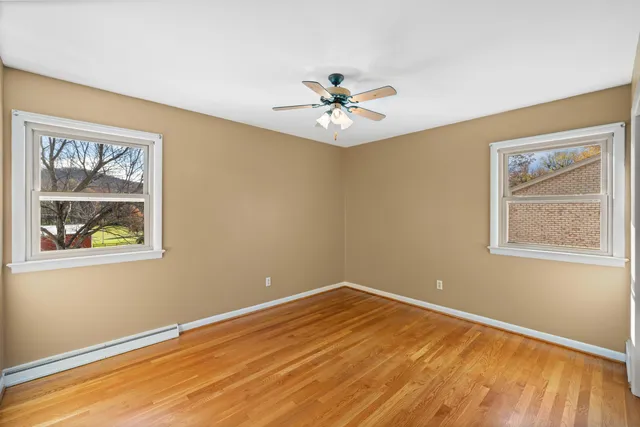 an empty room with wooden floor ceiling fan and windows