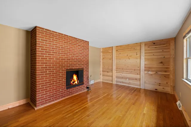 a view of an empty room with wooden floor fireplace and a window