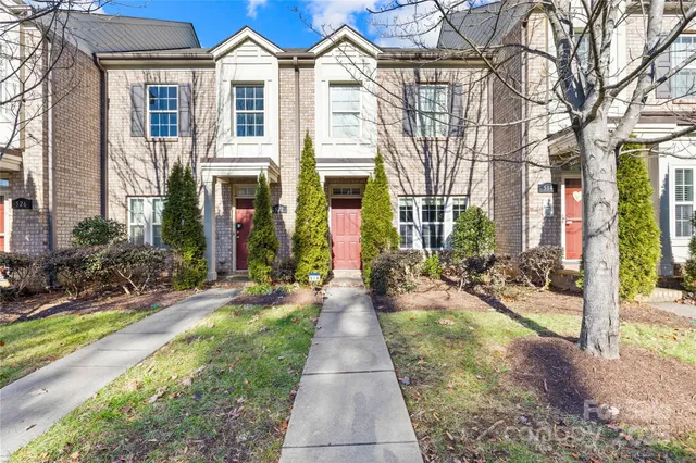 a view of a brick house with many windows plants and large tree