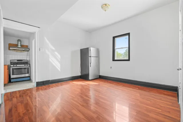 a view of empty room with wooden floor and kitchen