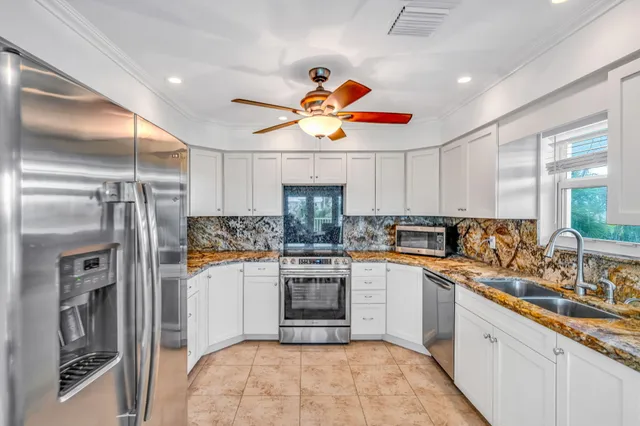 a kitchen with stainless steel appliances granite countertop a refrigerator a stove and white cabinets with wooden floor