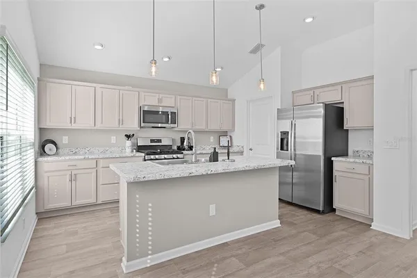 a kitchen with stainless steel appliances granite countertop a refrigerator a stove a sink and white cabinets with wooden floor