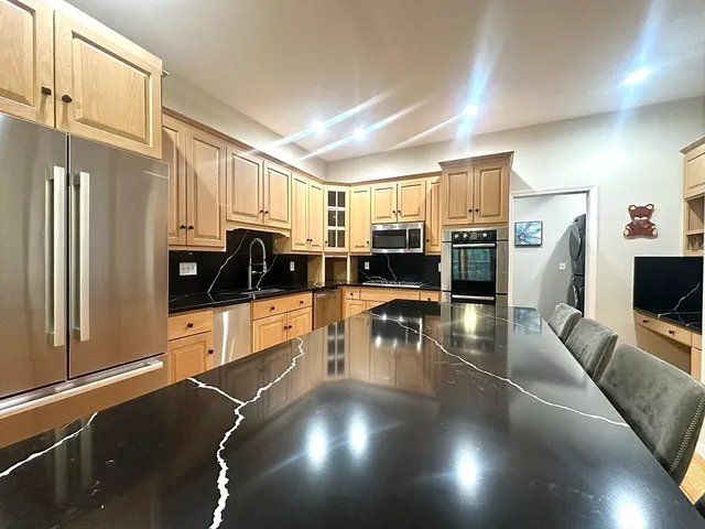 a kitchen with stainless steel appliances a refrigerator a stove a sink a dining table and chairs with wooden floor