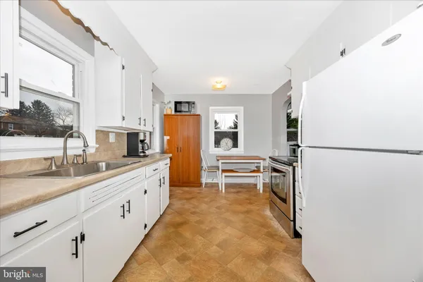 a kitchen with granite countertop a refrigerator a sink and white cabinets