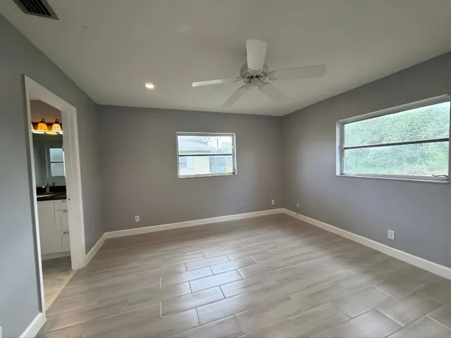 an empty room with wooden floor fan and windows