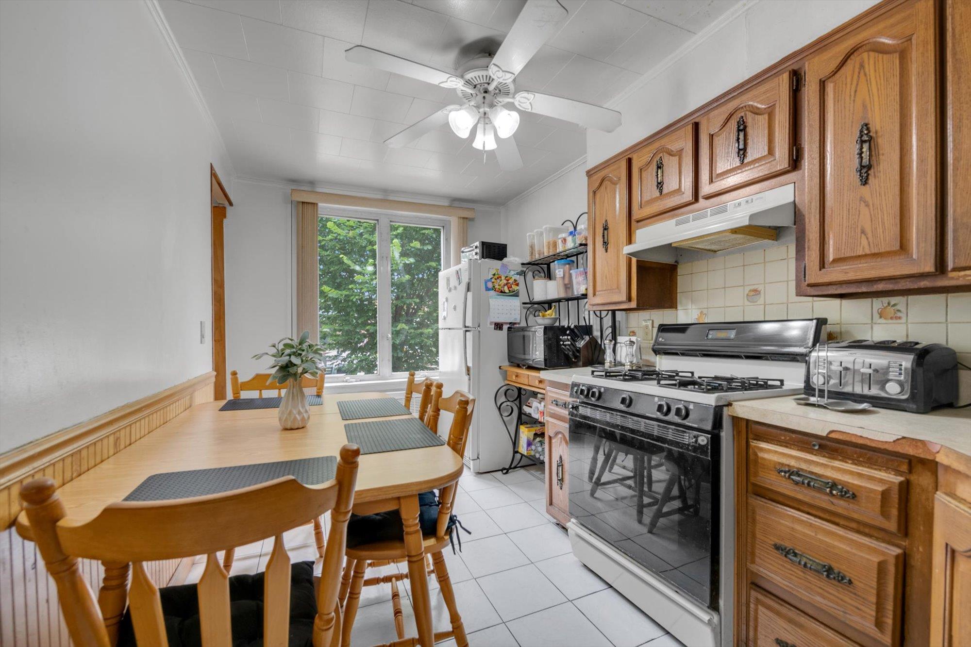 63-03 74th Street Queens, NY 11379 - Photo 6 of 15 Kitchen with white appliances, under cabinet range hood, crown molding, ceiling fan, and brown cabinetry