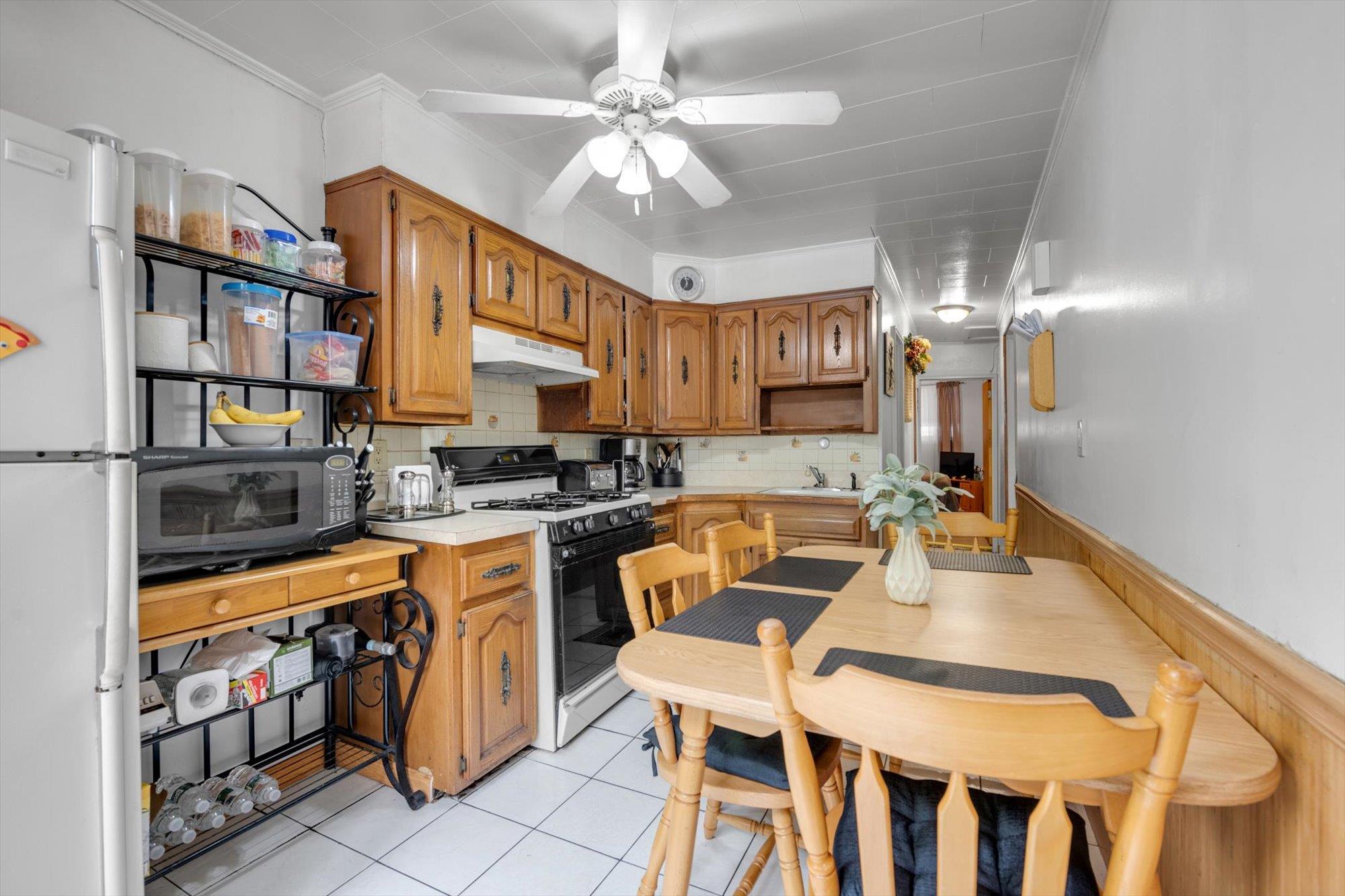 63-03 74th Street Queens, NY 11379 - Photo 7 of 15 Kitchen featuring black appliances, under cabinet range hood, a ceiling fan, light tile patterned floors, and light countertops