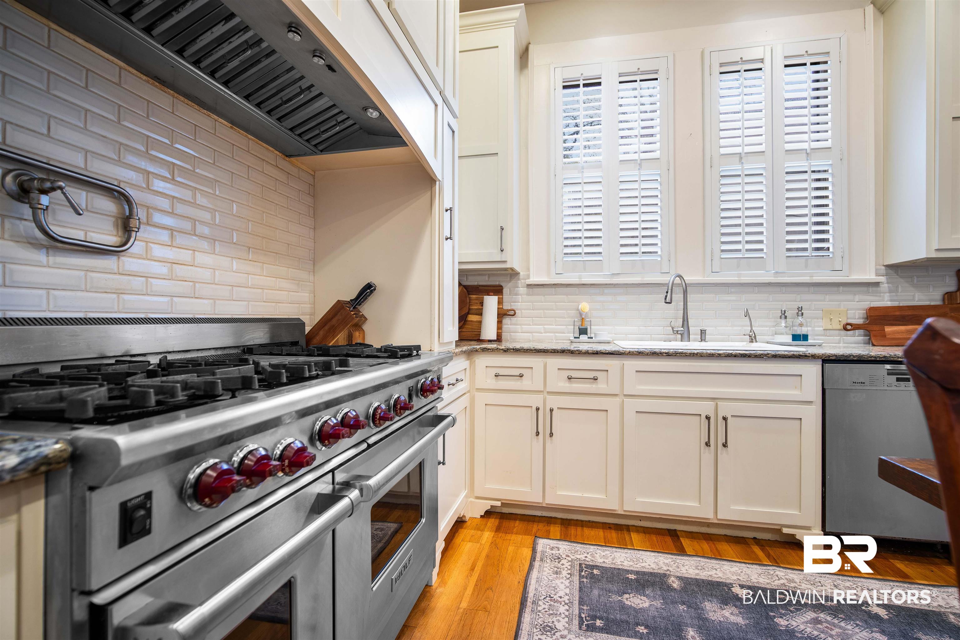 1314 Dauphin Street Mobile, AL 36604 - Photo 26 of 61 Kitchen featuring light stone counters, custom range hood, appliances with stainless steel finishes, and light hardwood flooring