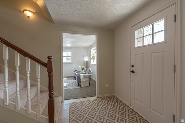 1045 Fox Farm Road Logan, UT 84321 - Photo 8 of 65 Foyer entrance featuring a textured ceiling, stairway, light colored carpet, and light tile patterned floors