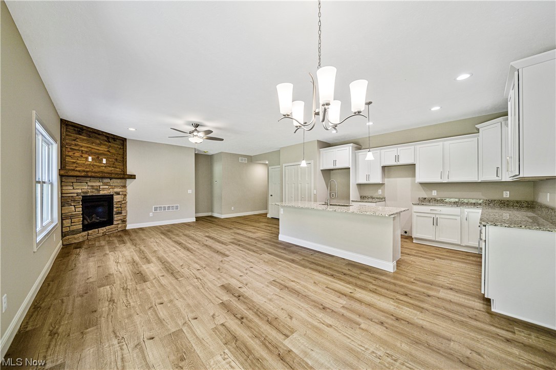 1745 Green Road Madison, OH 44057 - Photo 11 of 35 Kitchen featuring light hardwood / wood-style flooring, a stone fireplace, ceiling fan with notable chandelier, white cabinets, and a kitchen island with sink