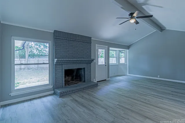 an empty room with windows fireplace and wooden floor