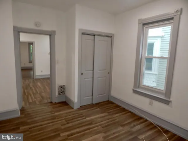an empty room with wooden floor closet and windows