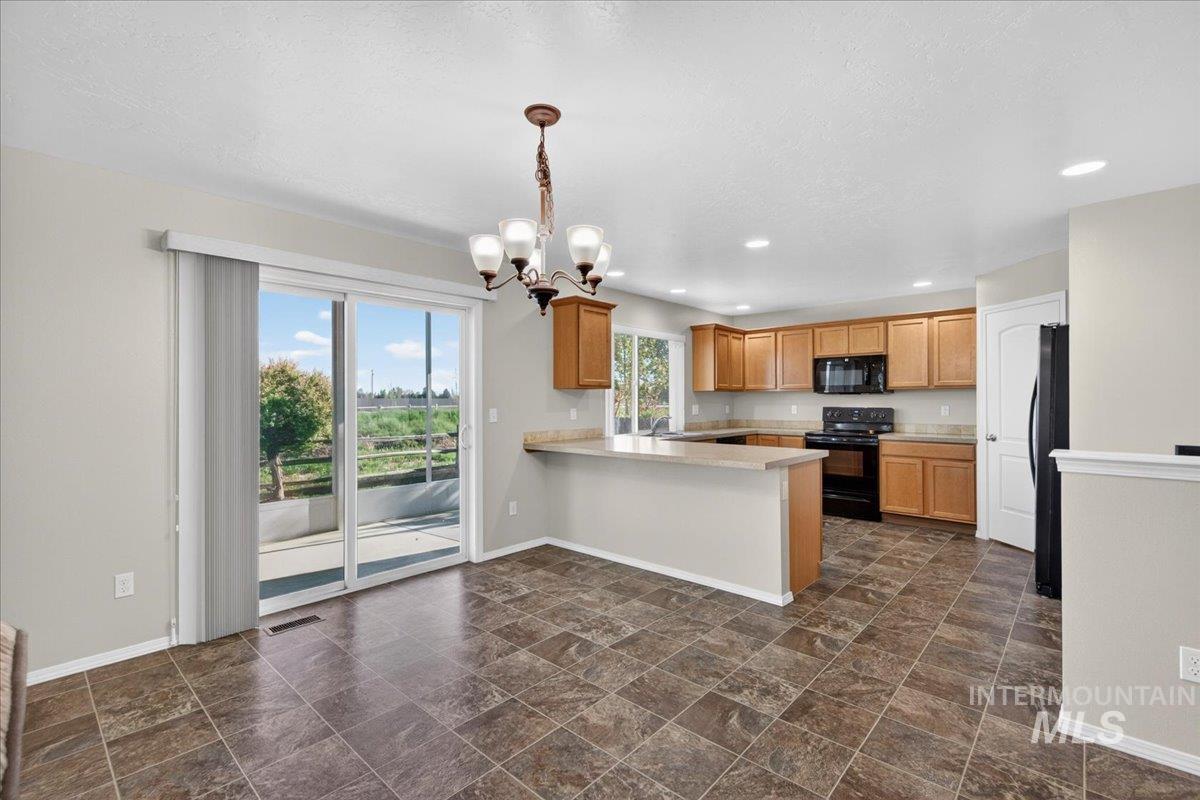 1555 Condor Drive Middleton, ID 83644 - Photo 8 of 50 Kitchen and dining space featuring wood-finish cabinetry, black appliances, a breakfast bar, recessed lighting, and sliding glass doors to the outdoor patio