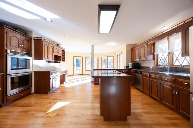 a kitchen with stainless steel appliances granite countertop a stove top oven a sink dishwasher a dining table and chairs with wooden floor