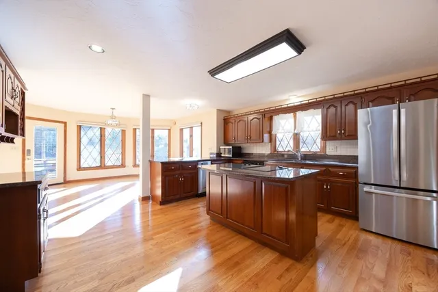 a kitchen with stainless steel appliances granite countertop a stove a refrigerator a sink and a large window with wooden floor