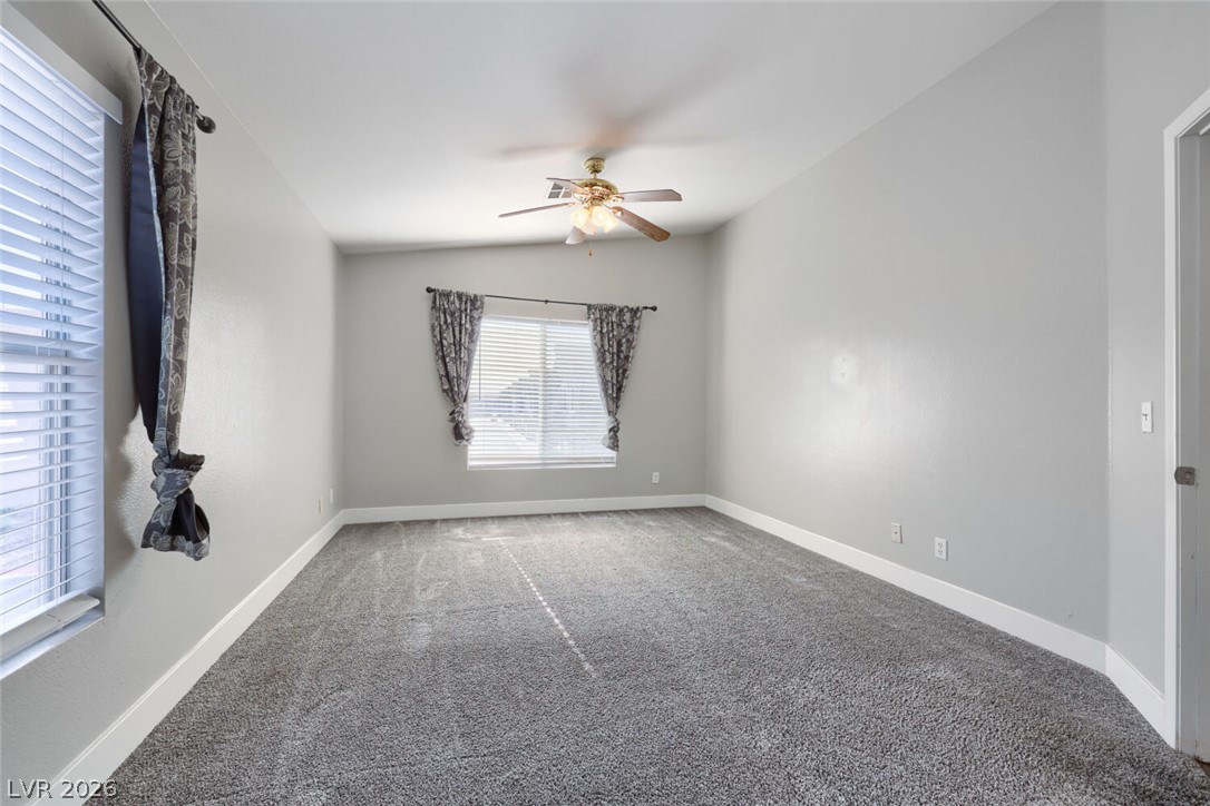 5985 High Steed Street, Unit 101 Henderson, NV 89011 - Photo 26 of 38 A spacious bedroom features soft carpeting, large windows, and a classic ceiling fan.