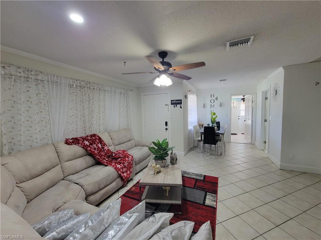 10 East Jersey Road Lehigh Acres, FL 33936 - Photo 12 of 32 Living room featuring visible vents, light tile patterned floors, ornamental molding, a ceiling fan, and a textured ceiling
