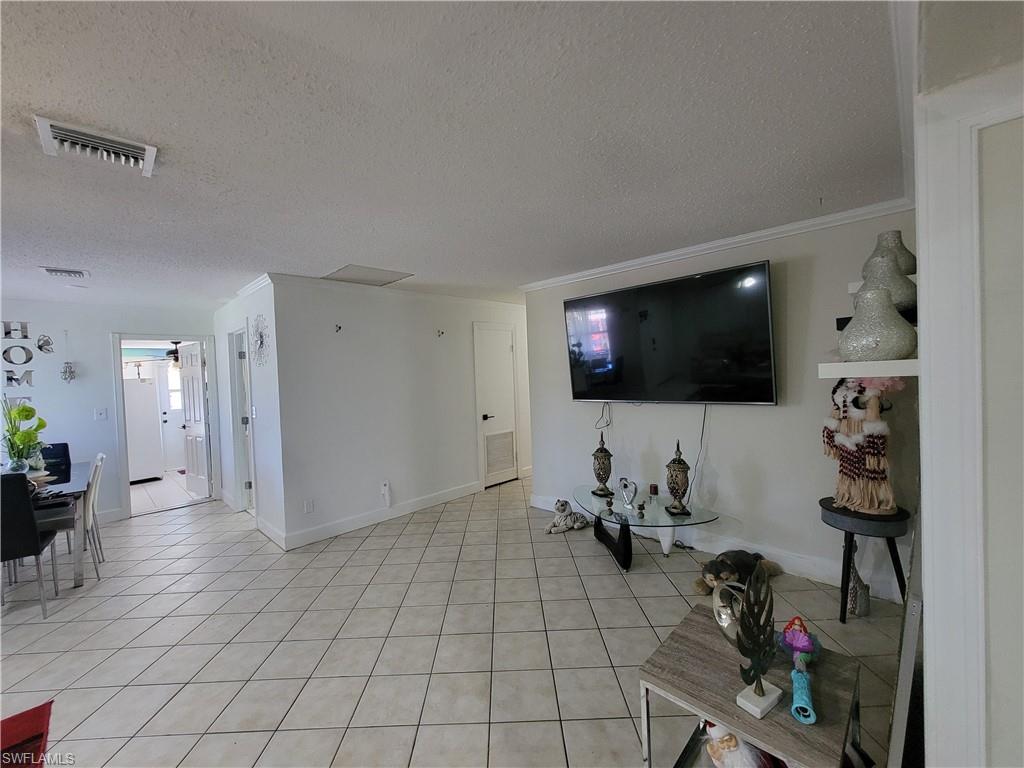 10 East Jersey Road Lehigh Acres, FL 33936 - Photo 13 of 32 Living room with a textured ceiling, light tile patterned floors, ornamental molding, and visible vents