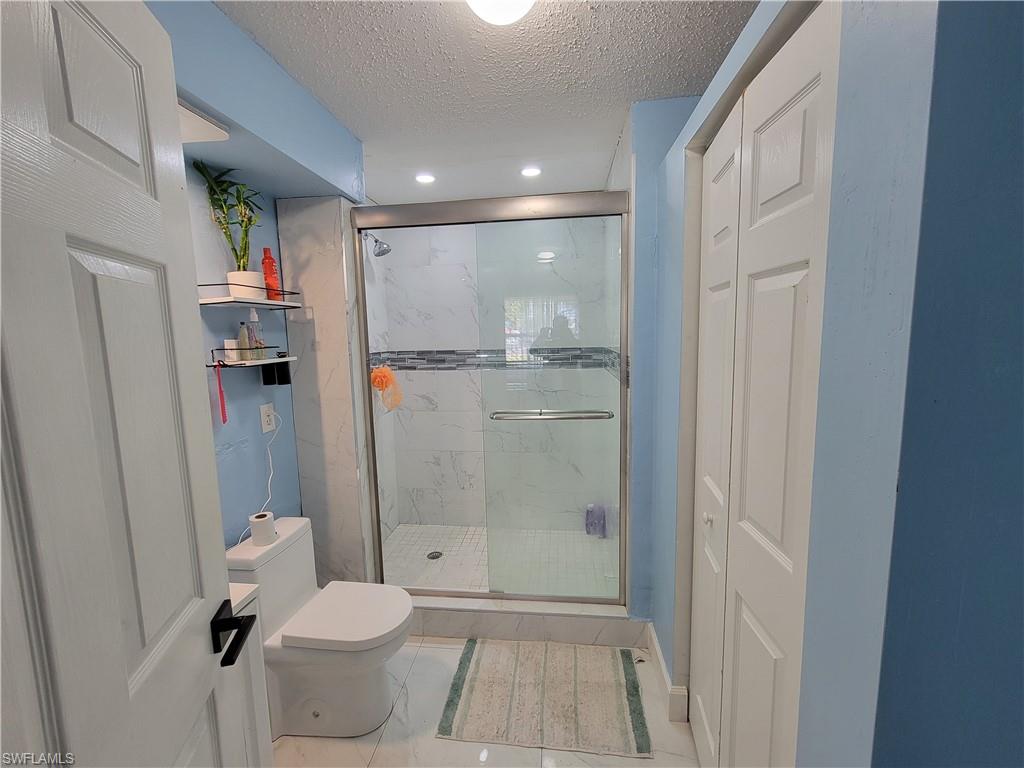 10 East Jersey Road Lehigh Acres, FL 33936 - Photo 15 of 32 Full bath with a marble finish shower, toilet, marble finish floor, and a textured ceiling