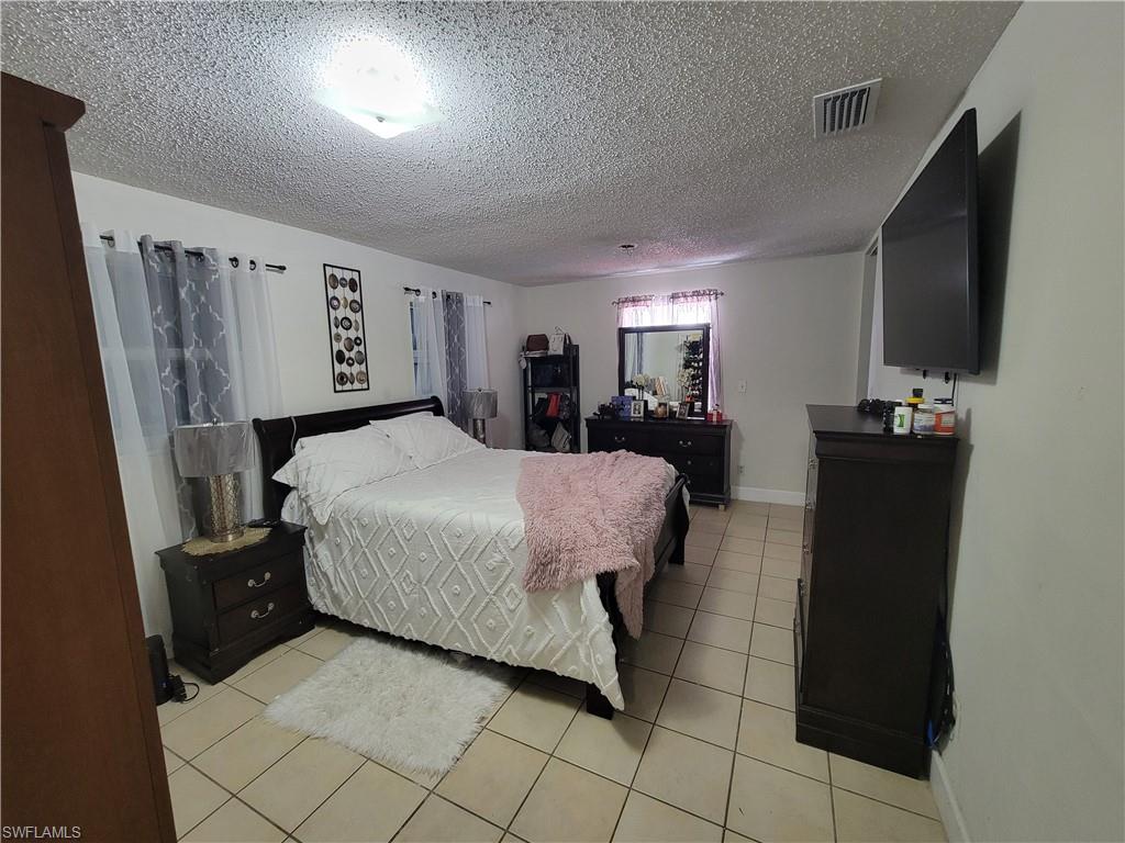 10 East Jersey Road Lehigh Acres, FL 33936 - Photo 20 of 32 Bedroom featuring light tile patterned floors, visible vents, a textured ceiling, and baseboards