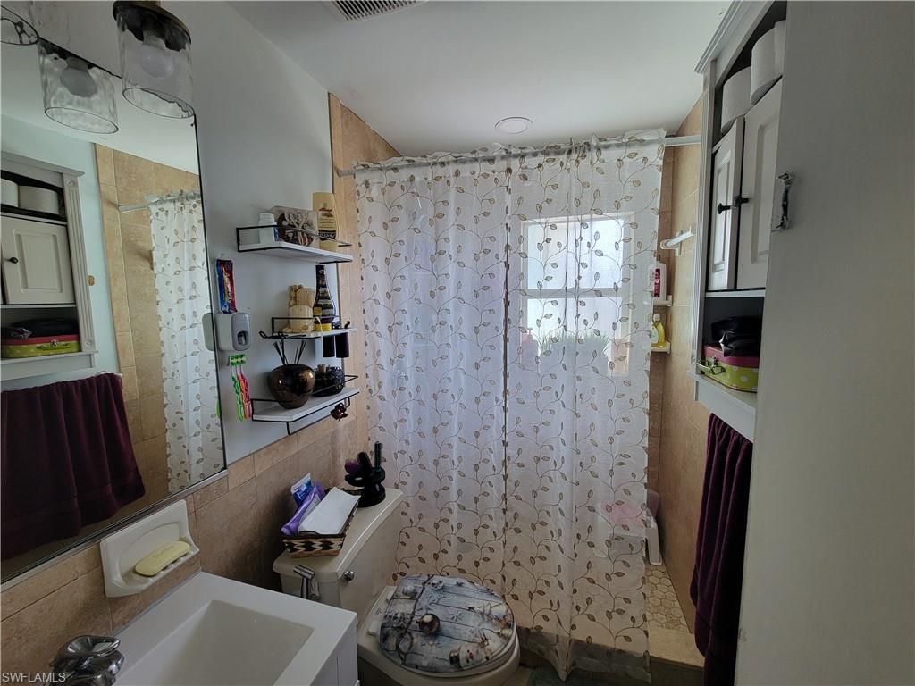 10 East Jersey Road Lehigh Acres, FL 33936 - Photo 22 of 32 Full bathroom featuring a shower with curtain, visible vents, and tile walls
