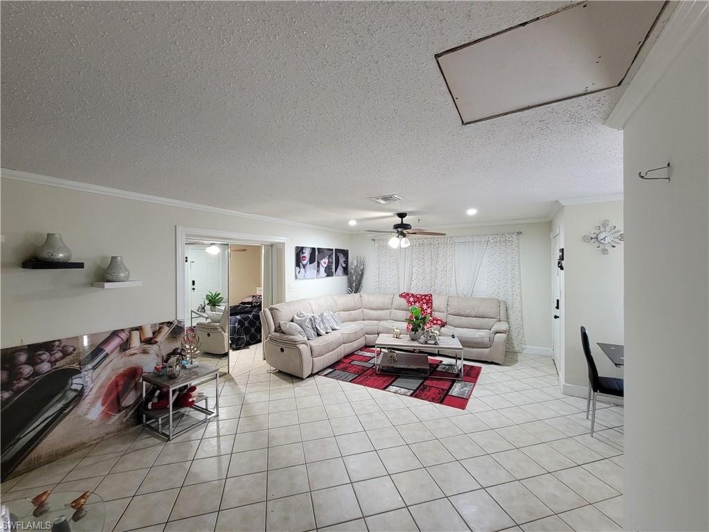 10 East Jersey Road Lehigh Acres, FL 33936 - Photo 10 of 32 Living area featuring baseboards, light tile patterned floors, a textured ceiling, crown molding, and visible vents