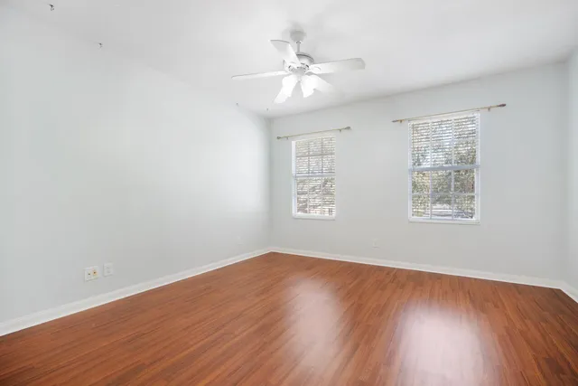 an empty room with wooden floor chandelier fan and windows