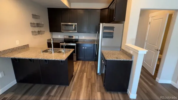 a kitchen with kitchen island granite countertop stainless steel appliances stove microwave refrigerator and wooden floor