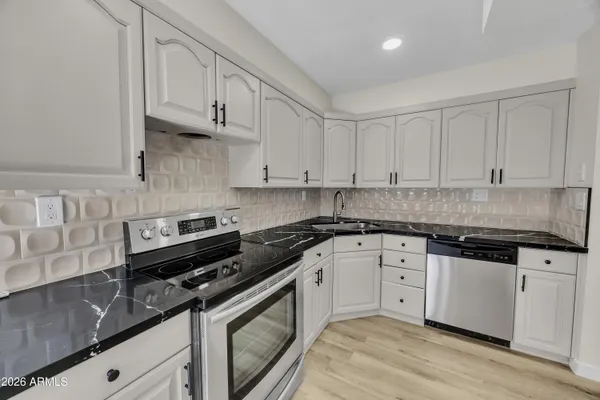 a kitchen with stainless steel appliances granite countertop a stove a sink and white cabinets
