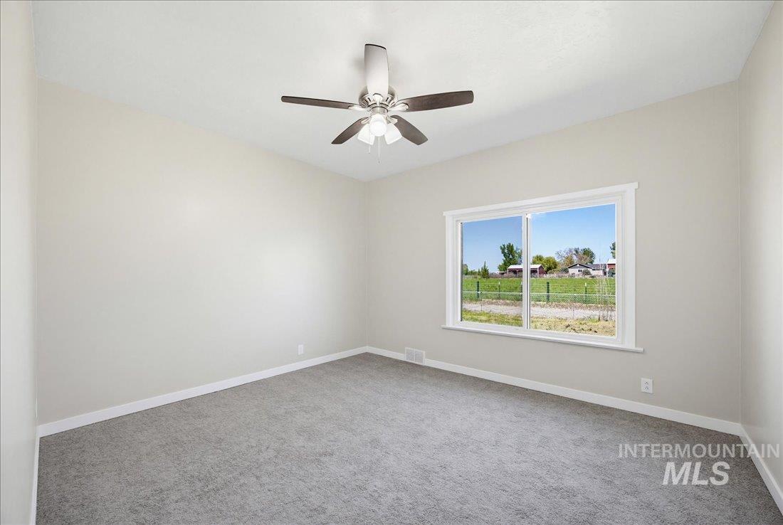 30013 Apple Valley Road Parma, ID 83660 - Photo 20 of 25 Light-filled room featuring neutral wall tones, gray carpeting, a multi-pane window with white trim, and a ceiling fan with integrated lighting