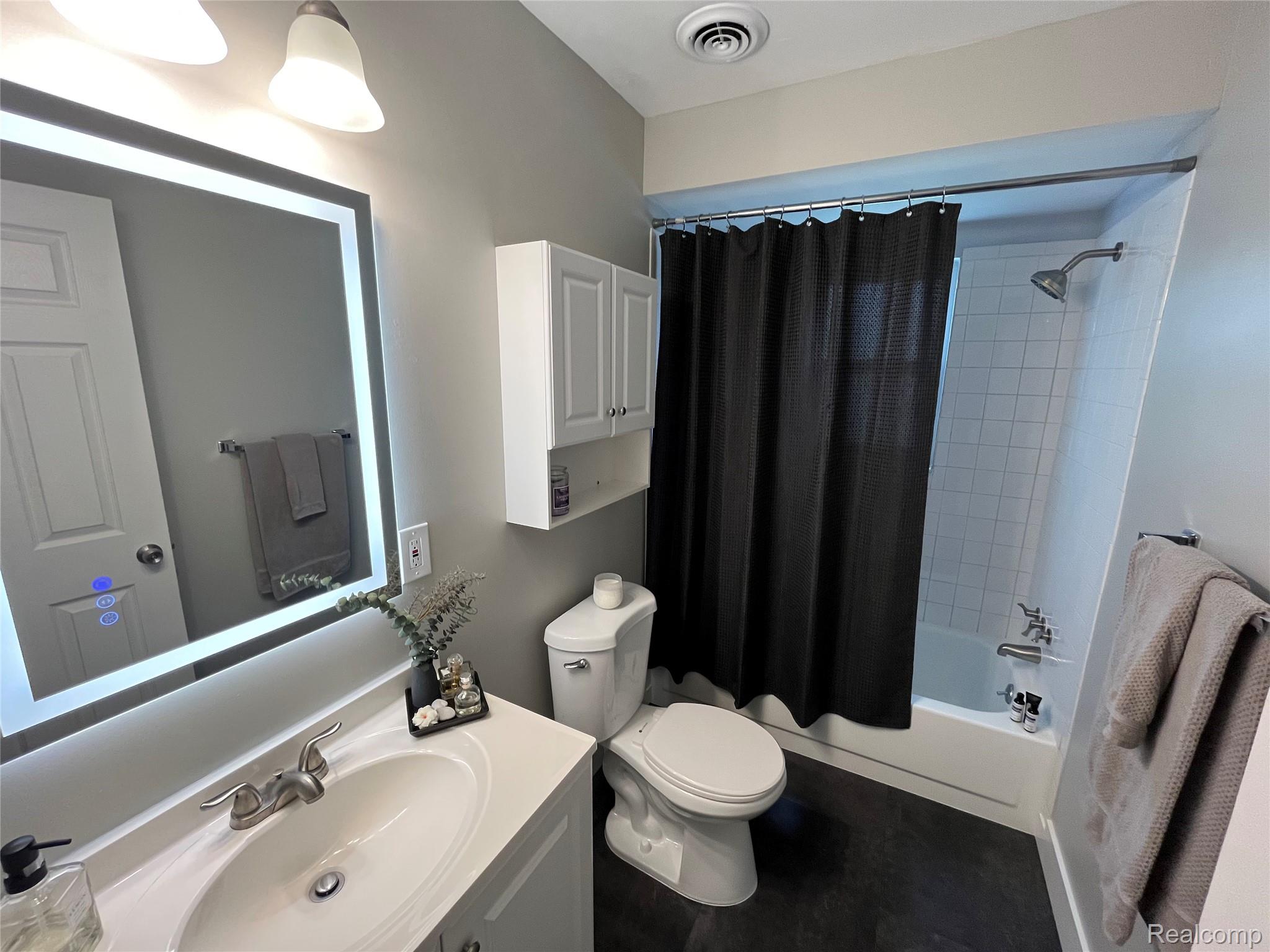 2639 Columbia Road, Unit 7 Berkley, MI 48072 - Photo 8 of 8 Bathroom featuring an illuminated vanity mirror, a single-basin vanity with brushed nickel fixtures, a built-in wall cabinet, a toilet, and a tiled tub-shower combination