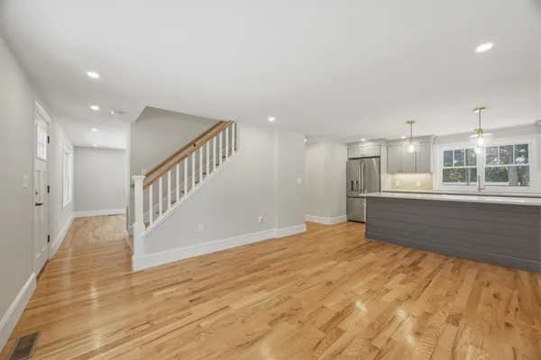 a view of an empty room with wooden floor and a kitchen