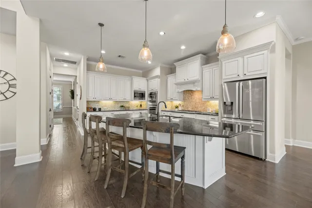 a kitchen with stainless steel appliances kitchen island granite countertop a dining table chairs refrigerator and microwave